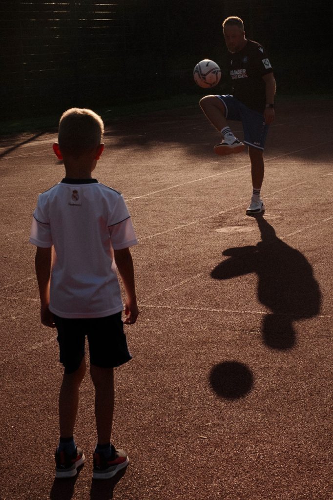 Martin spielt mit seinem Sohn Fußball auf dem Bolzplatz